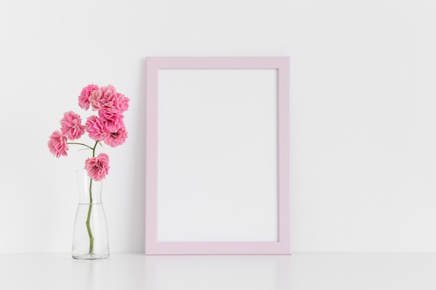 Maquette de cadre rose avec des roses roses dans un vase en verre sur une table blancheOrientation portrait