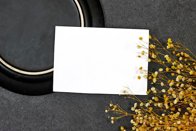 Photo maquette de carte d'invitation de mariage au-dessus d'une plaque de céramique noire avec de la gypsophile sur fond gris