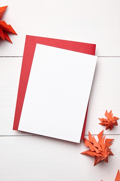 Maquette de carte de Noël avec enveloppe et sapins en papier rouge sur fond de bois blanc vue de dessus mise à plat