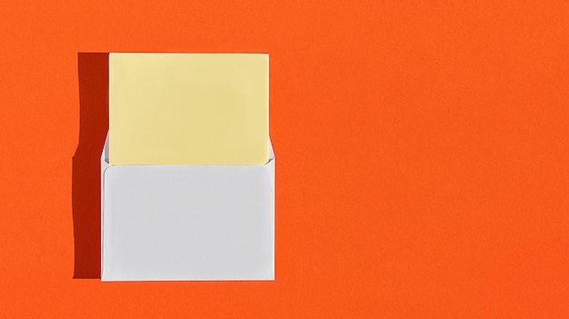 Maquette de carte postale avec enveloppe blanche et papier à lettres jaune vierge sur fond orange brûlé. Concept créatif, modèle de carte de voeux. Disposition horizontale avec espace de copie