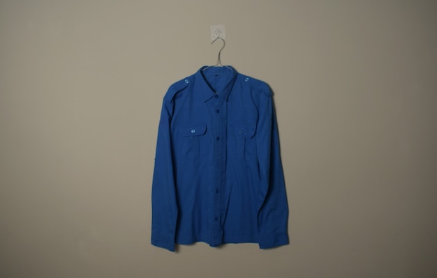 Maquette de chemise extérieure bleue à manches longues vierge sur cintre sur la vue latérale avant du mur de fond