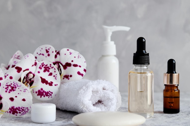 Photo maquette de cosmétiques pour le corps et le visage huiles essentielles bouteilles de crème savon serviette et fleurs d'orchidées