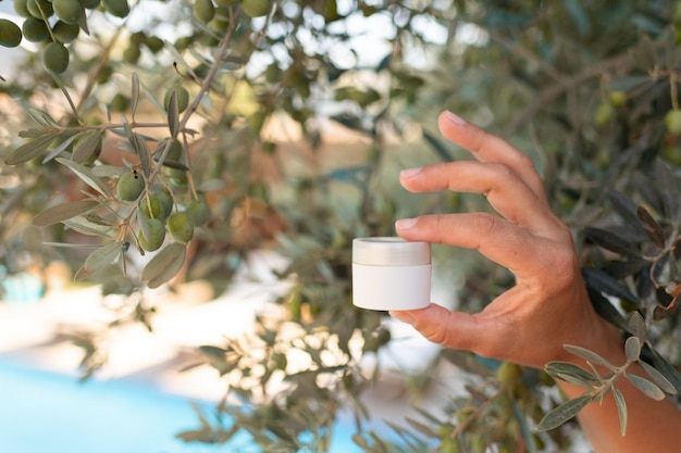 Maquette de crème pour la peau, tube blanc dans les mains féminines sur fond d'olivier, sécurité de la peau