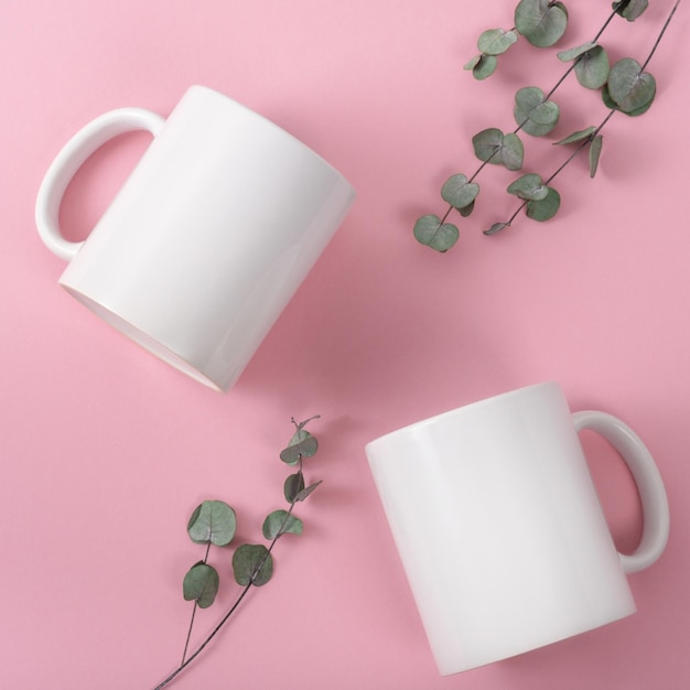 Maquette de deux tasses ou tasses à café blanches sur fond rose avec espace de copie. Modèle vierge pour votre conception, image de marque, entreprise. Vrai photo. Branches d'eucalyptus à plat