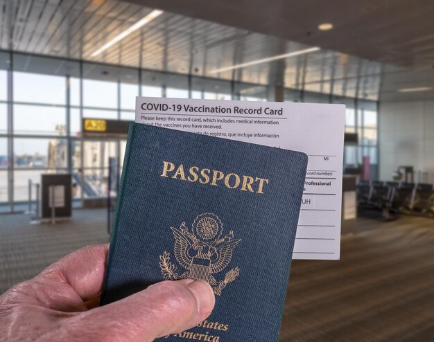 Maquette du terminal de l'aéroport avec la main d'un homme d'affaires tenant un passeport américain et un certificat de vaccination contre le coronavirus