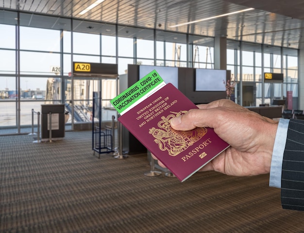 Maquette du terminal de l'aéroport avec la main d'un homme d'affaires tenant un passeport britannique et un certificat de vaccination contre le coronavirus