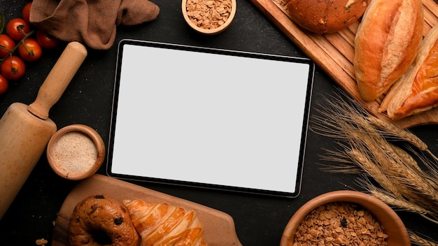 Une maquette d'écran vide de pavé tactile de tablette numérique sur une table de pâtisserie de boulangerie. Fond de pain cuit au four