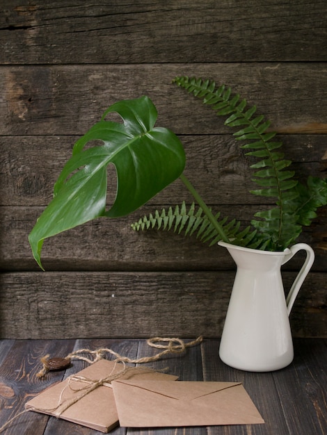 Maquette d&#39;espace de travail avec des feuilles tropicales dans des enveloppes de vase et d&#39;artisanat sur fond en bois