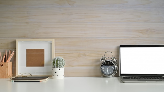 Photo maquette espace de travail ordinateur portable maquette, cadre photo, réveil et cactus sur le bureau avec mur en bois.