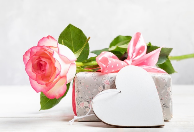 Maquette festive avec boîte-cadeau enveloppée dans du papier floral doux rose rose coeur en bois blanc vide