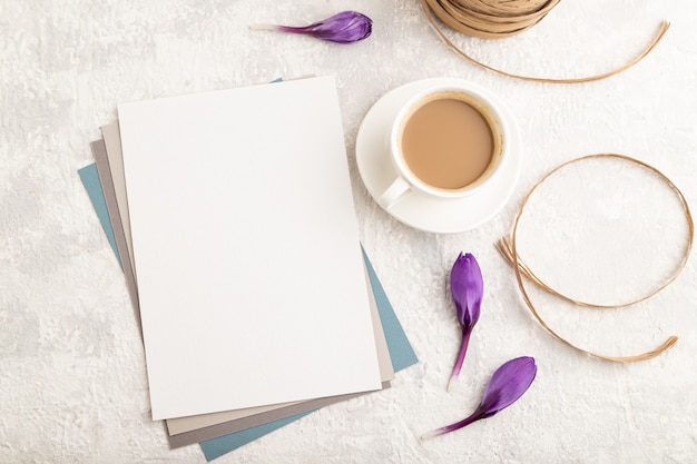 maquette de feuille de papier blanc avec des fleurs de crocus printanières et une tasse de café sur fond de béton gris.