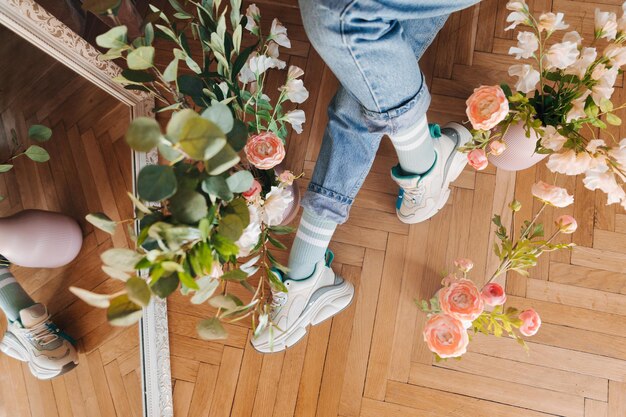 Maquette en gros plan Jambes d'une fille en jeans et baskets au milieu de la vue de dessus de fleurs