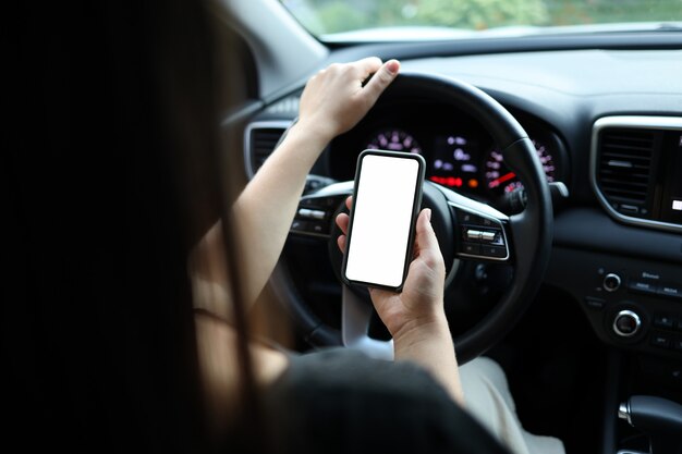 Maquette d'image, fille utilisant un téléphone intelligent mobile à écran blanc vierge à l'intérieur d'une voiture par temps ensoleillé, écran tactile ou texto, espace de copie pour votre publicité