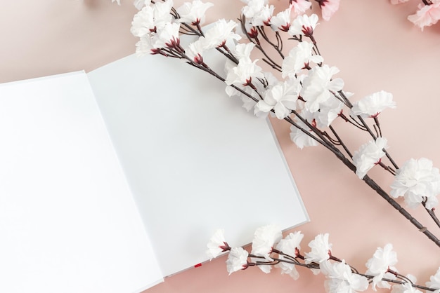 Maquette de livre blanc ouvert sur fond rose pastel avec fleur de cerisier blanche et rose.
