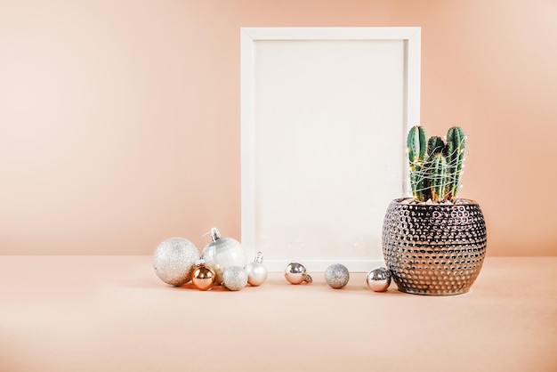 Maquette de Noël avec cadre blanc, cactus et boules de Noël sur fond pastel