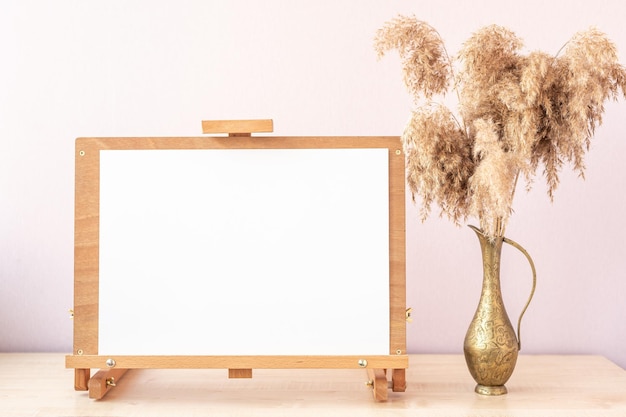 Maquette de papier blanc sur chevalet en bois et vase avec roseaux sur table au home studio