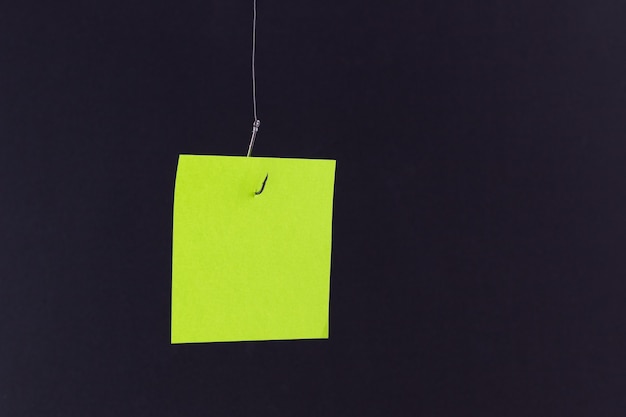 Maquette d'un papier mémo vert vierge avec espace de copie accroché à un hameçon de pêche