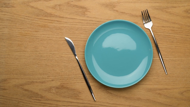 Maquette plaque en céramique, fourchette et couteau de table sur table en bois, vue de dessus, assiette propre, plat en céramique vide, arrière-plan de réglage de la table