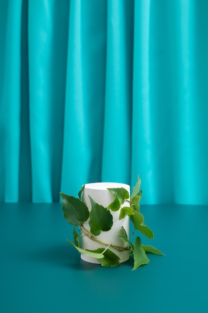 Maquette de podium ou de piédestal avec des feuilles pour la production cosmétique sur un fond turquoise avec des plis de tissu.