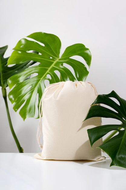 Maquette de sac écologique réutilisable pour des achats zéro déchet parmi les feuilles vertes de monstera minimal tendance compo ...