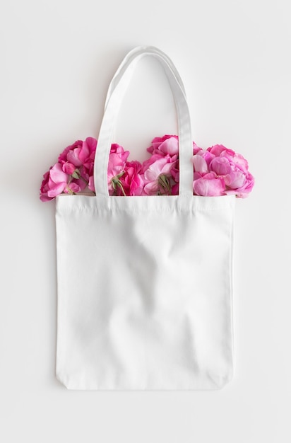 Maquette de sac fourre-tout blanc avec un bouquet de roses sur un tableau blanc