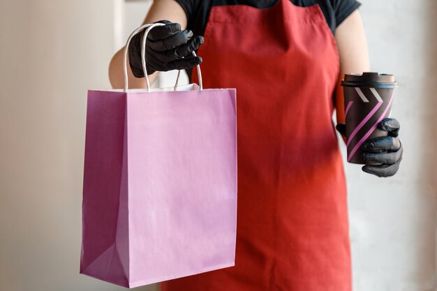 Maquette de sac en papier violet pour aliments à emporter. Verrouillage de la livraison de nourriture sans contact covid 19. Sac de nourriture, paquet de tasse de café à emporter dans un restaurant à emporter. L'employé de cuisine donne des commandes de gants et de masques.