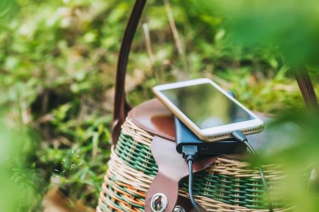 Maquette d'un smartphone avec chargeur Power Bank sur un panier dans la forêt. Concept sur le thème des loisirs de plein air.