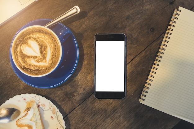 Maquette de smartphone avec écran blanc mobile sur le bureau en bois au café