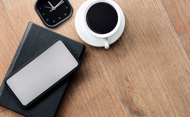 Maquette smartphone écran blanc avec tasse de café et réveil sur plancher en bois