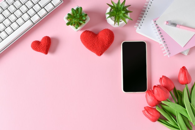 Une maquette d'un smartphone avec des tulipes et des coeurs tricotés un clavier sur fond rose Les blogueurs et aiment la carte de voeux Saint Valentin avec des coeurs sur fond rose