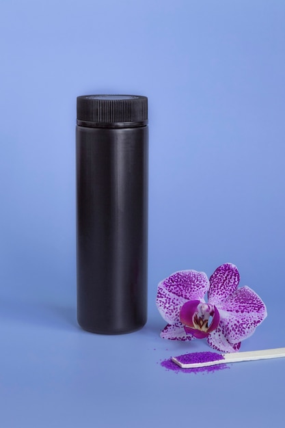 Maquette de spa : spa cosmétique violet au sel de mer, bouteille en plastique noir avec du sel, orchidée violette sur fond bleu.