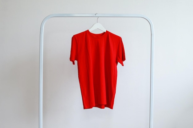 Une maquette de t-shirt de couleur rouge sur un cintre blanc suspendu à des vêtements de rack.