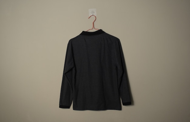 Maquette de t-shirt décontracté à manches longues noir vierge sur cintre sur fond de mur vue latérale arrière
