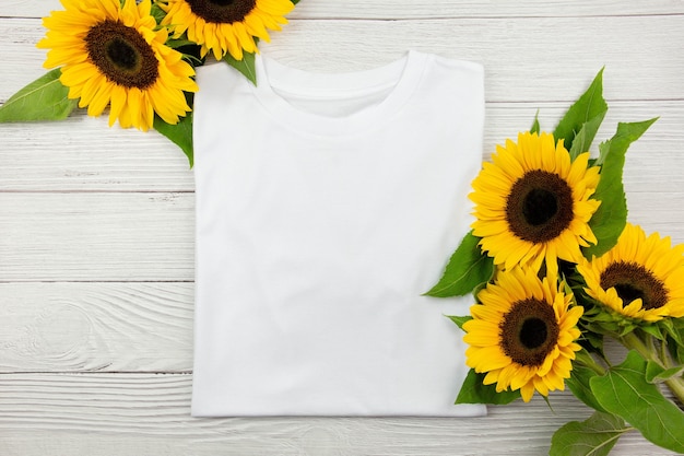 Maquette de T-shirt plié en coton pour femmes blanches avec des tournesols sur fond de bois blanc. Concevoir un modèle de t-shirt, une maquette de présentation imprimée. Vue de dessus à plat.