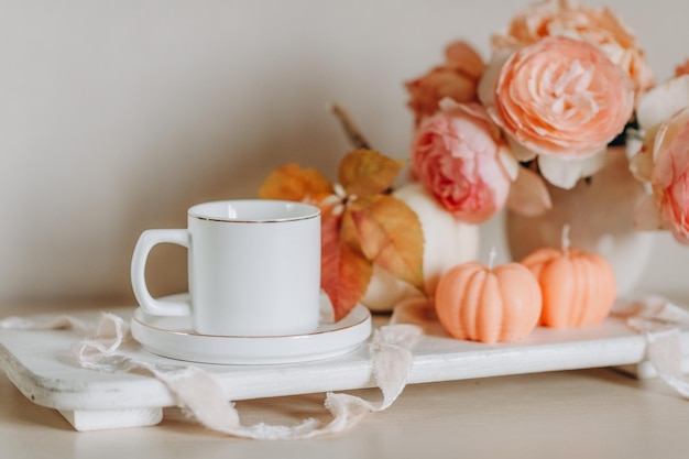 maquette d'une tasse blanche sur fond de bougies, roses, citrouilles, dans des tons roses