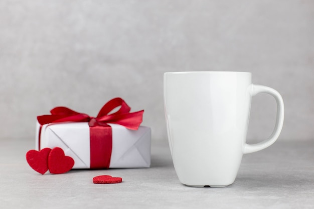 Maquette de tasse blanche vierge avec boîte-cadeau et coeurs rouges, pierre de béton léger.