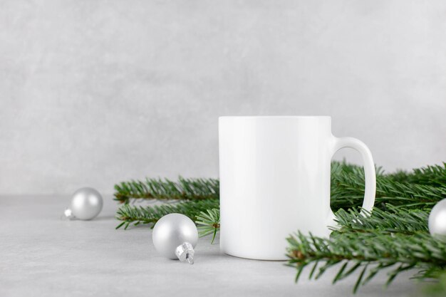 Maquette de tasse blanche vierge avec des branches d'arbres de Noël et des boules d'argent sur fond de pierre en béton clair Composition de vacances Vue latérale Espace de copie