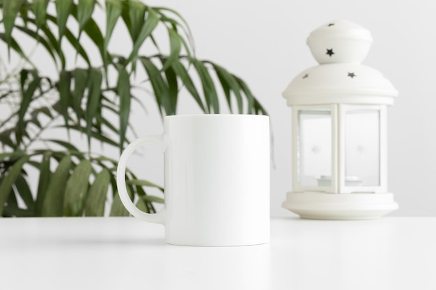 Maquette de tasse avec un bougeoir sur une table blanche avec une plante de palmier