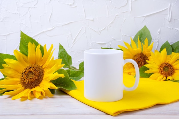 Maquette de tasse à café blanche avec tournesols et serviette jaune sur la table en bois. Mug vide maquette pour la promotion du design, modèle stylé