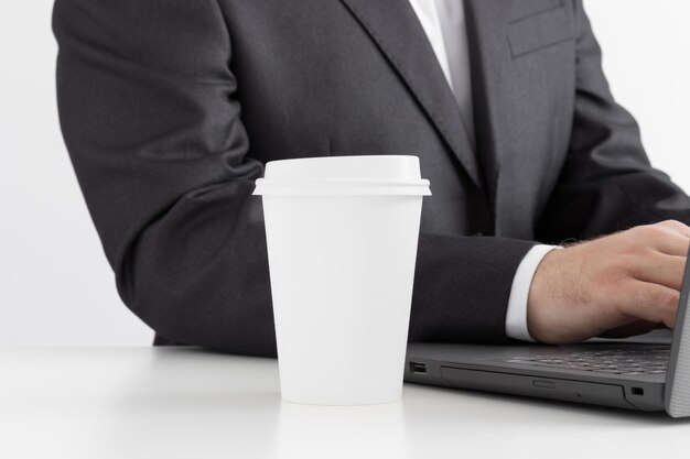 Maquette de tasse de café en papier blanc avec un homme travaillant sur un ordinateur