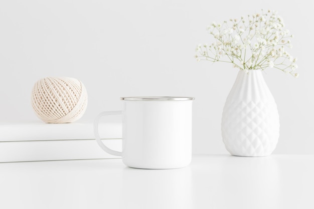 Photo maquette de tasse en émail avec accessoires d'espace de travail et une gypsophile sur un tableau blanc