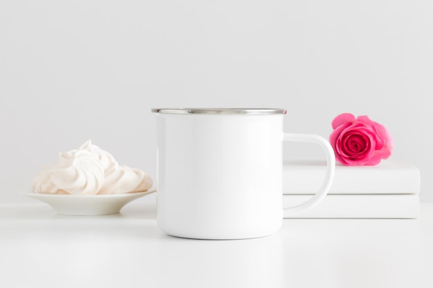 Maquette de tasse en émail avec des livres et une rose rose sur un tableau blanc