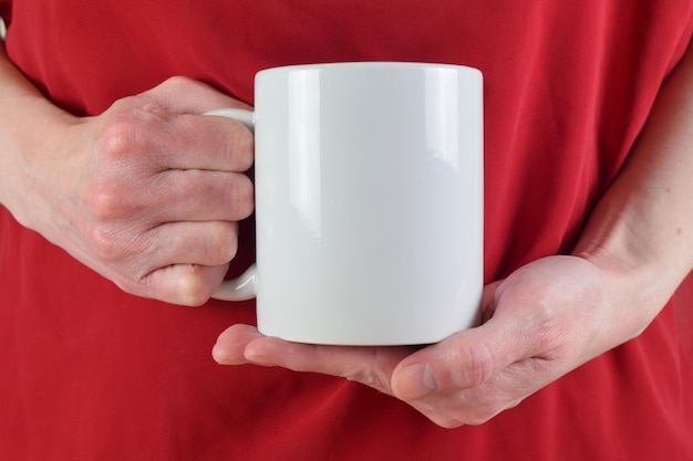 Photo maquette de tasse avec une femme tenant une tasse blanche de 11 oz contre un chemisier rouge