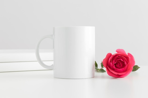 Maquette de tasse avec des livres et une rose rose sur un tableau blanc