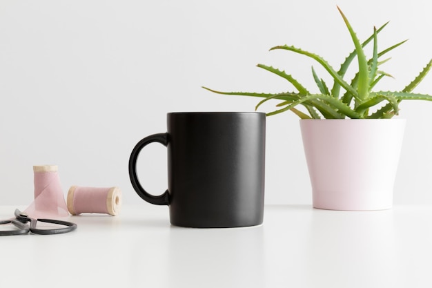 Maquette de tasse noire avec une plante d'aloe vera et des accessoires d'espace de travail sur un tableau blanc