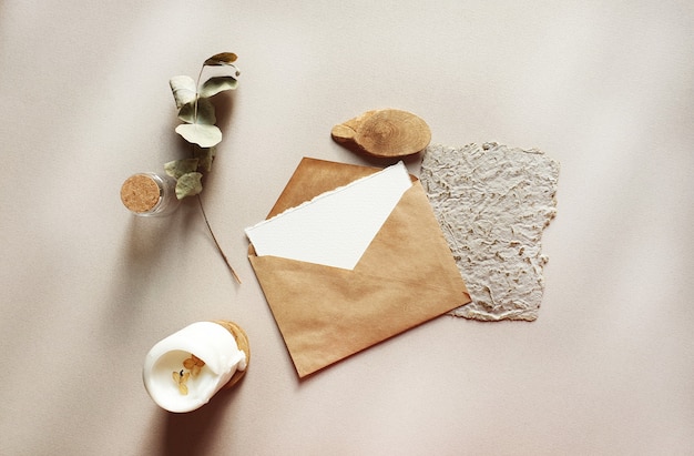 Maquettes de cartes d'invitation de voeux de mariage blanc vierge avec enveloppe d'artisanat, feuilles d'eucalyptus séchées sur fond de table texturé. Modèle moderne élégant pour l'identité de marque. Mise à plat, vue de dessus