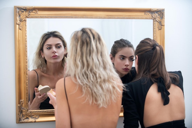 Le maquillage applique les cosmétiques Copines femmes appliquant le maquillage se préparant pour la fête regardant dans le miroir