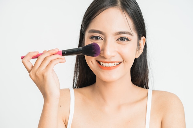 Maquillage beauté femme asiatique souriant gros plan. Belle jeune femme appliquant une poudre de fond de teint ou un fard à joues avec un pinceau de maquillage. Modèle de race mixte asiatique caucasien.