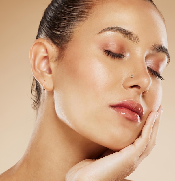 Maquillage beauté et visage d'une femme avec une lueur de cosmétiques sur un fond de studio marron Soins de la peau et jeune modèle cosmétique touchant l'art du visage avec un glam naturel pour l'élégance du visage