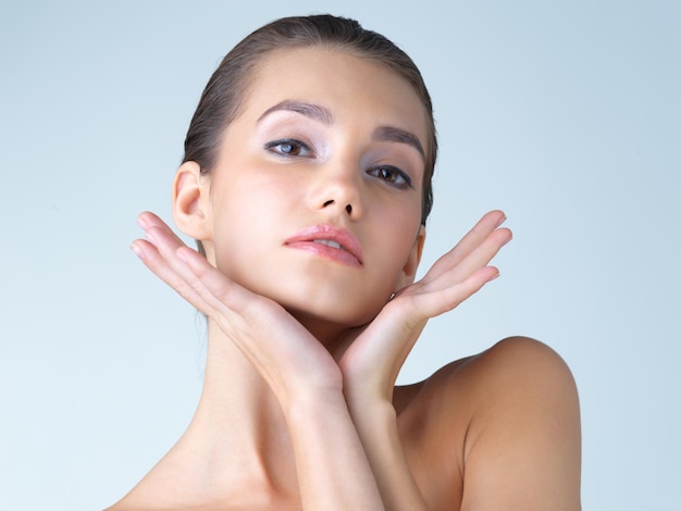 Maquillage femme et mains sur le visage en studio pour le bien-être des soins de la peau ou cosmétique sur fond bleu Portrait modèle beauté et fille avec satisfaction dermatologique ou routine de peau de luxe tout en étant isolé